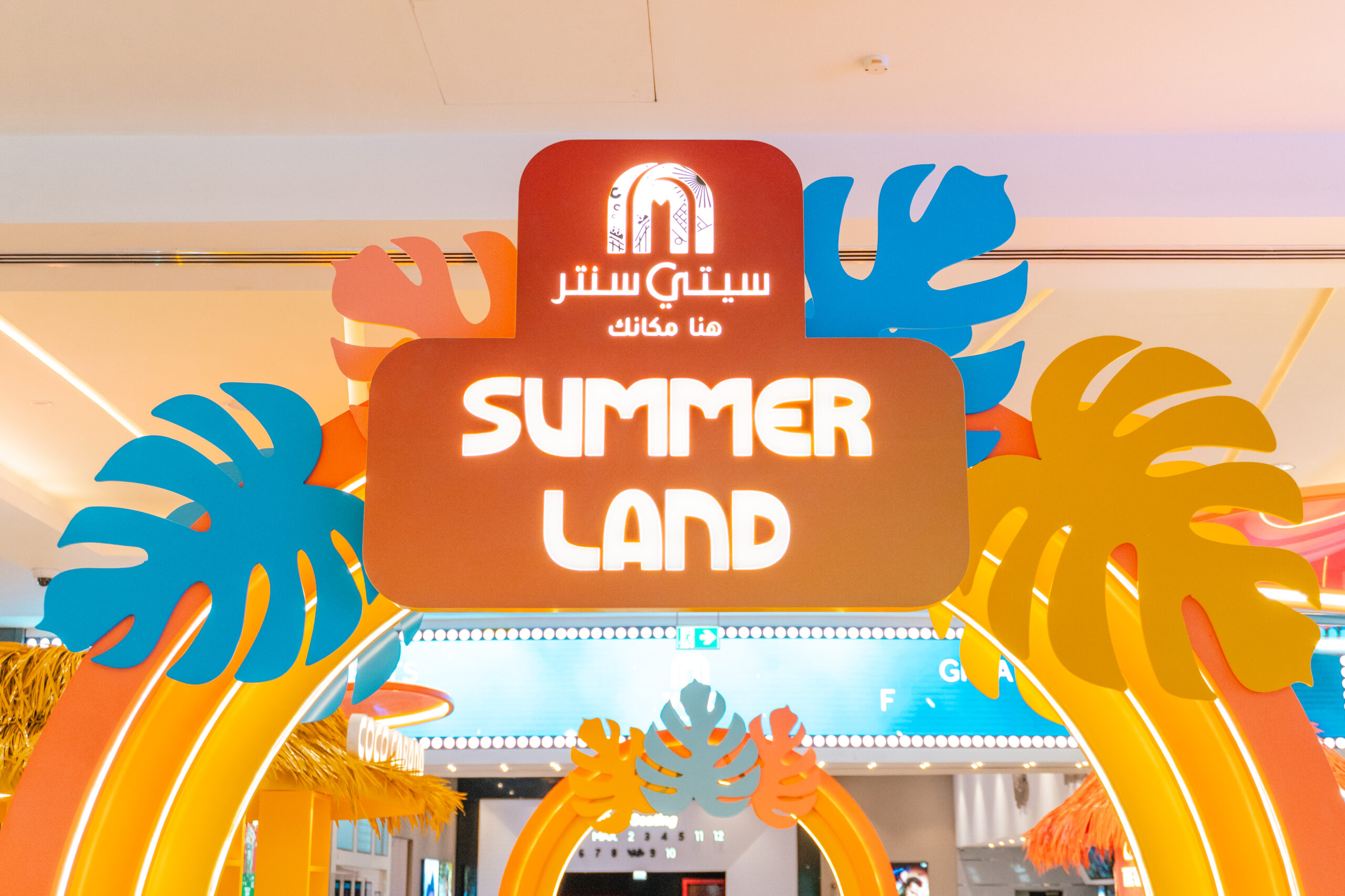 The Summer Land entrance sign under the City Centre logo, framed by cut-out leaves in coral and blue