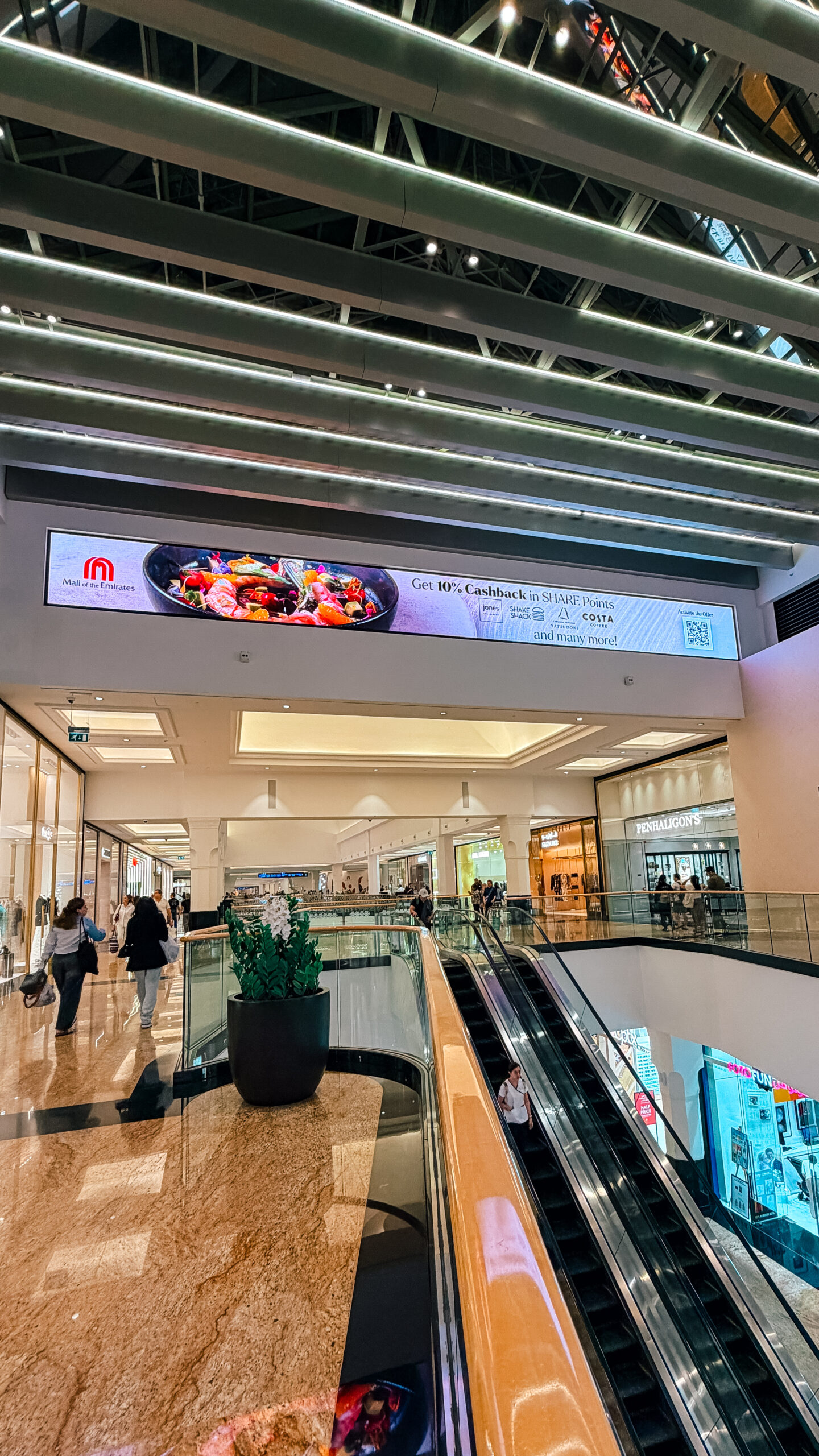 A slim SHARE Points cashback screen above the escalators in the skylit wing of Mall of the Emirates.