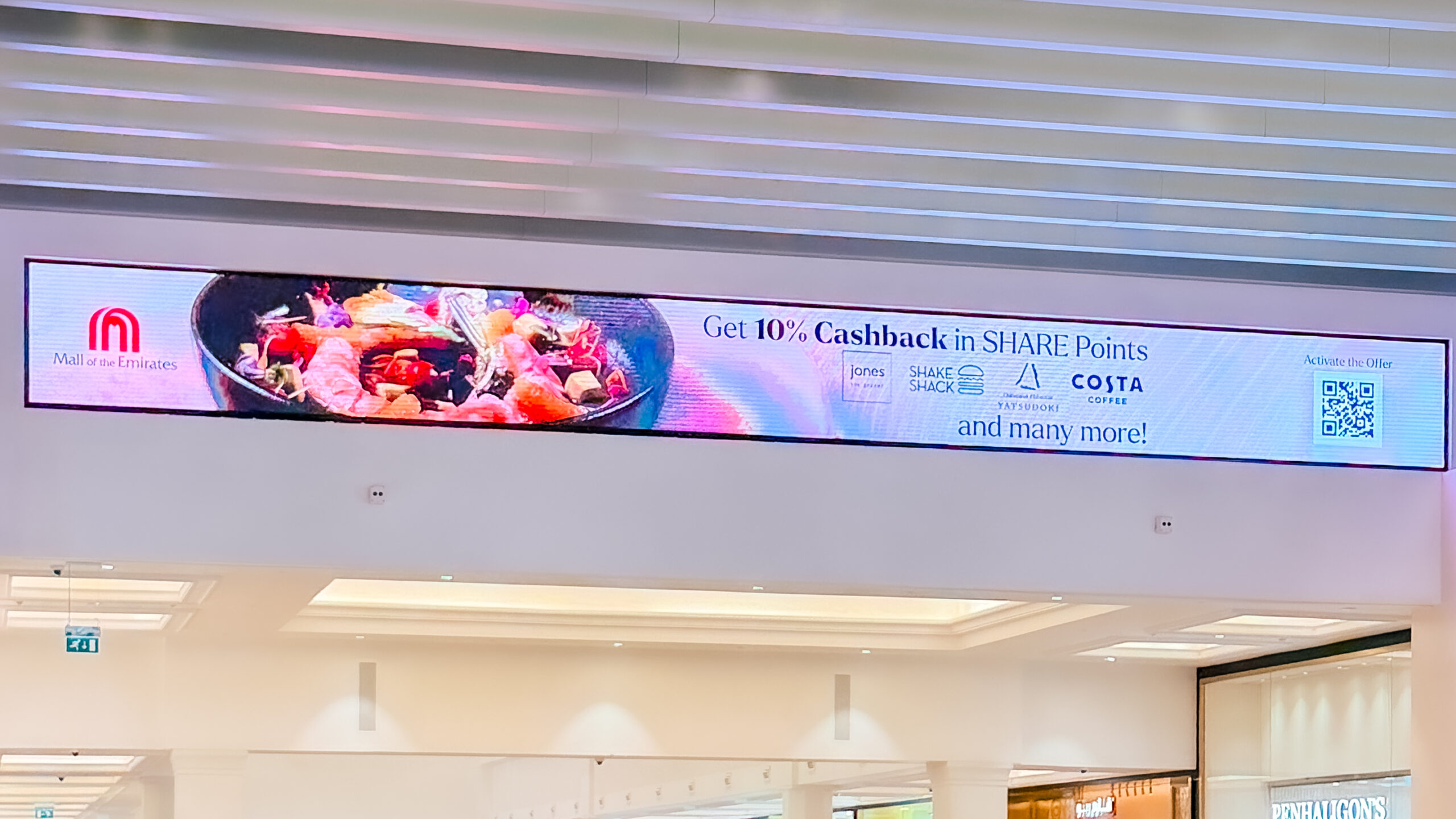 A slim SHARE Points cashback banner screen mounted along a ceiling beam at Mall of the Emirates.